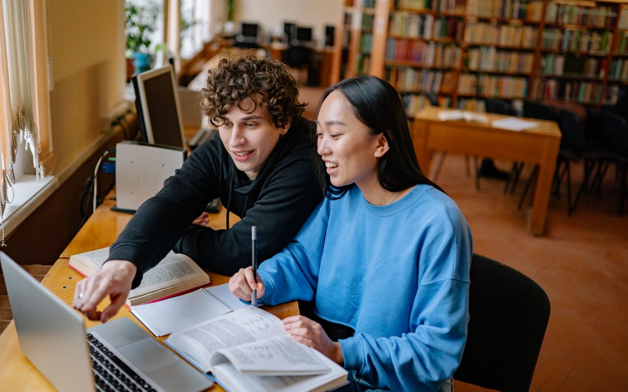 Estudantes fazendo anotações e pesquisando juntos na biblioteca