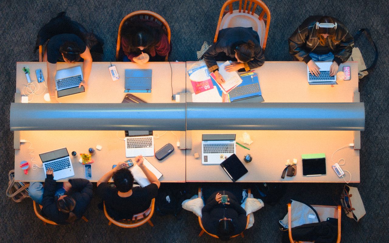 Grupo de estudantes trabalhando com cadernos e computadores em uma biblioteca