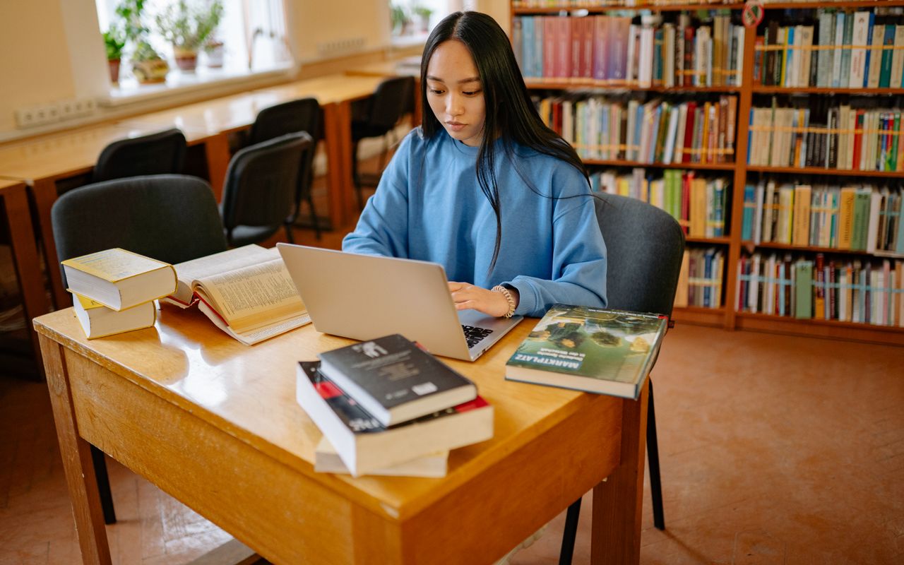 Estudante concentrada usando caderno e computador em uma biblioteca